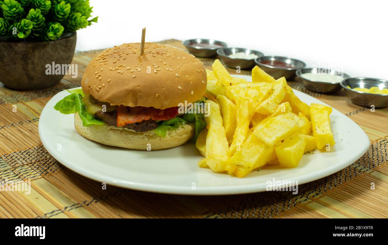 Weiße Platte mit Fleischburger, Speck und Salat, begleitet von pommes frites und mit Soßen in kleinen Platten auf weißem Grund Stockfoto