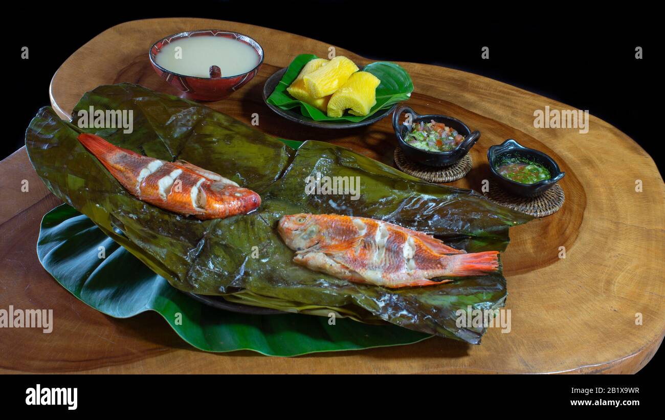 Gerichte mit Fisch Maitos, typische Gerichte des ecuadorianischen Amazonas, begleitet von Maniok, gekochten Bananen und Salat auf einem rustikalen Holztisch auf schwarzem BA Stockfoto