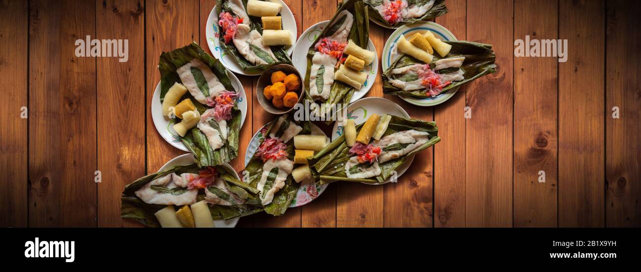 Blick auf Gerichte mit Fisch Maitos, typische Gerichte des ecuadorianischen Amazonas, begleitet von Maniok, gekochten Bananen und Salat auf einem Holztisch Stockfoto