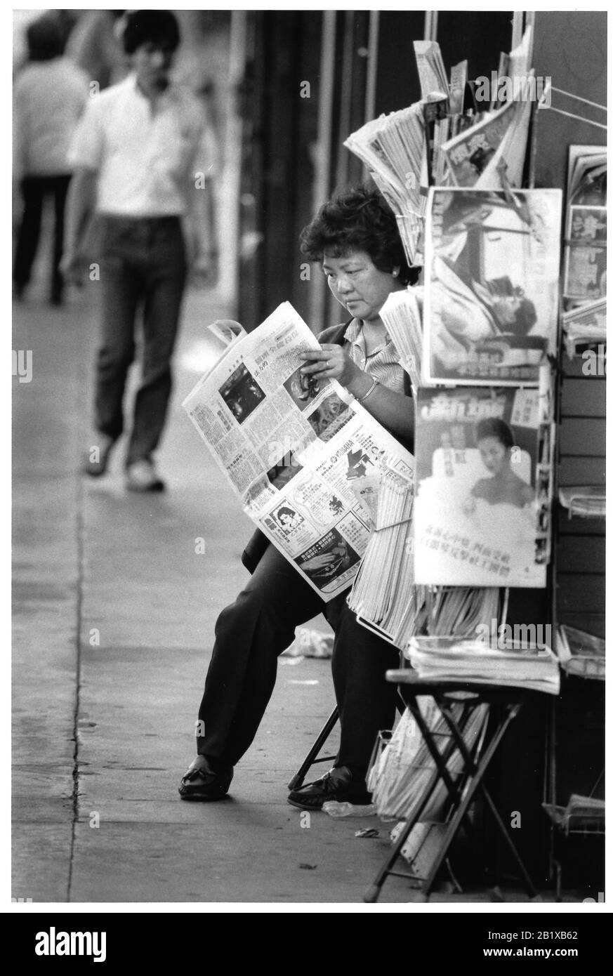 Asiatische Seniorin aus China liest am Nachmittag eine Zeitung in Los Angeles Chinatown auf der Straße vor ihrem Geschäft Stockfoto