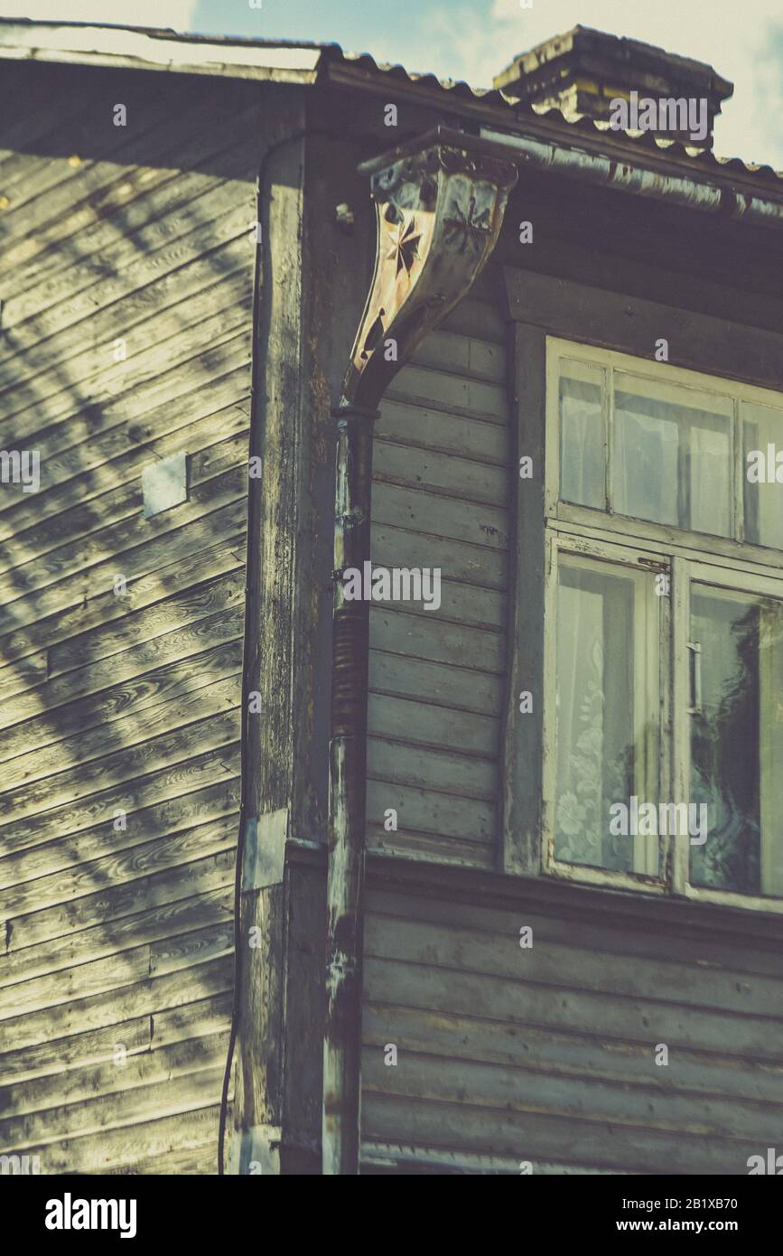 Einsames Fenster eines alten Holzhauses mit horizontaler Beplankung in der Ecke des zweiten Stocks und rostiger Regenwasserablaufleitung mit interessanten Mustern Stockfoto