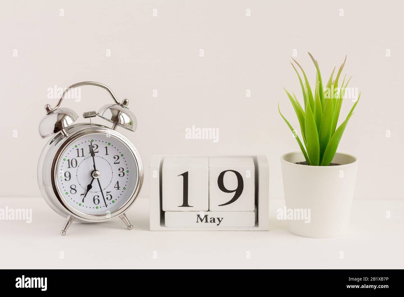 19. Mai auf einem Holzkalender neben einem Wecker und einer Blume. Ein Tag des Frühlingsmonats, Kalender und Wecker auf hellem Hintergrund. Frühling i Stockfoto