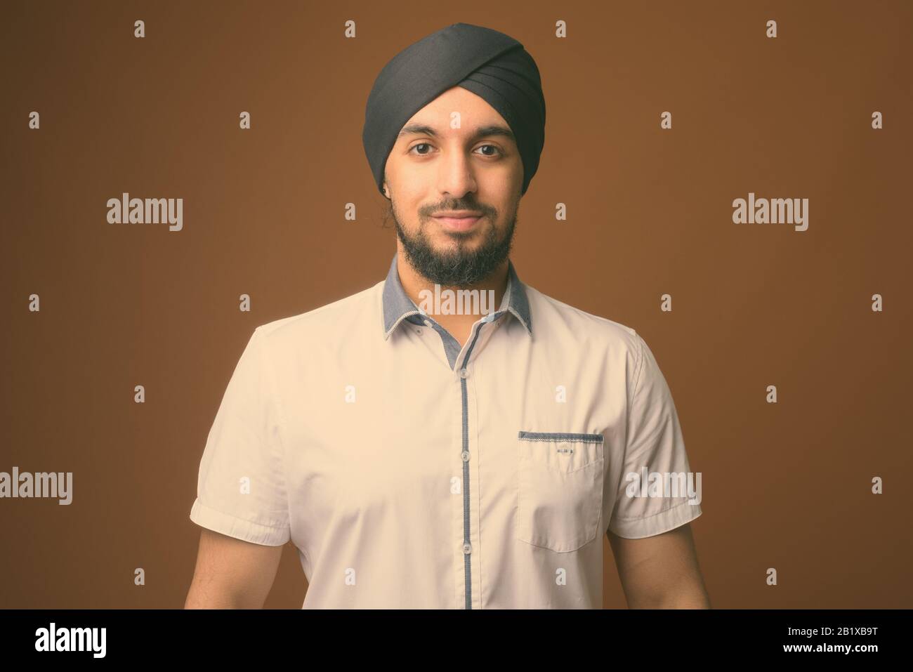 Studio erschossen Der junge Bartgeier indischen Sikh Mann, Smart Casual Kleidung gegen braunen Hintergrund Stockfoto