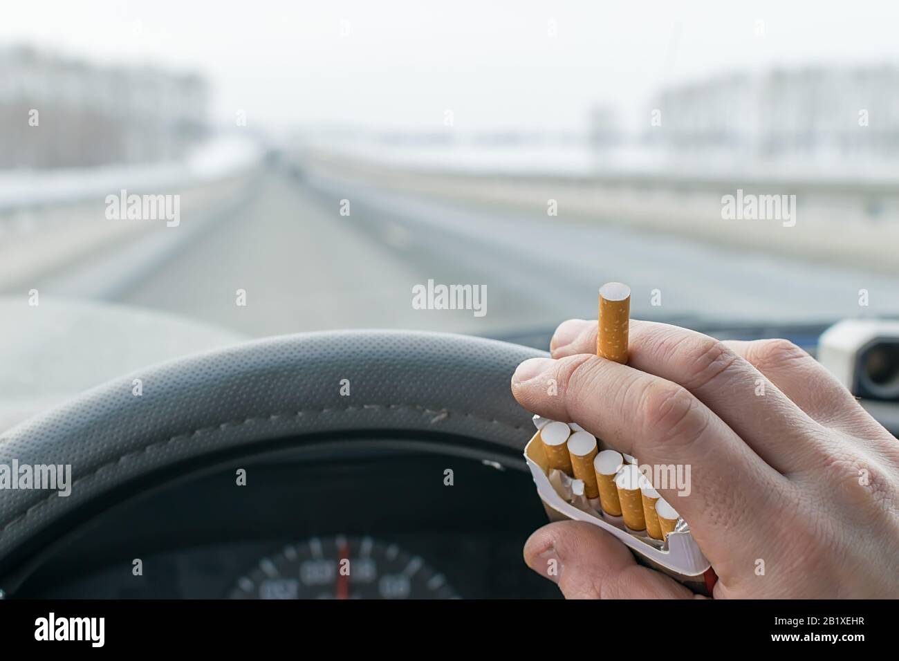 Blick auf die Hand eines Autofahrers, der während der Fahrt auf der Autobahn eine Packung Zigaretten hält Stockfoto