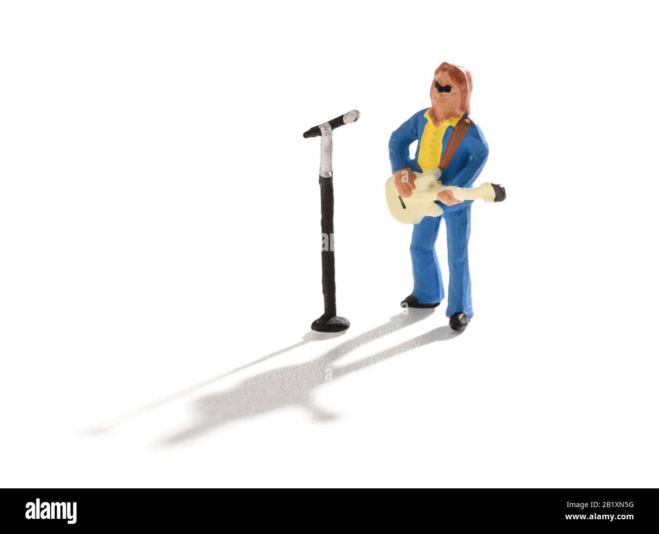 Miniaturgitarrist und Sänger stehen vor einem mike, der während eines Live-Auftritts auf Weiß mit Schatten singt Stockfoto