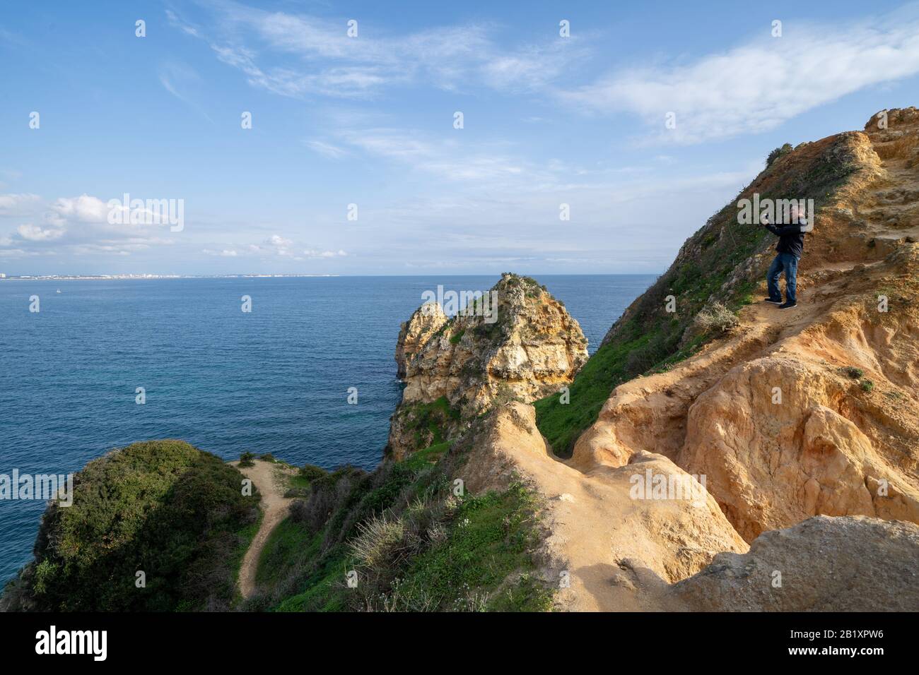 Lagos, Portugal - 22. Januar 2020: Thrillseeker Tourist man fotografiert mit einem Telefon auf einer sehr steilen Felswand an der Algarve, mit malerischen Aussichten Stockfoto