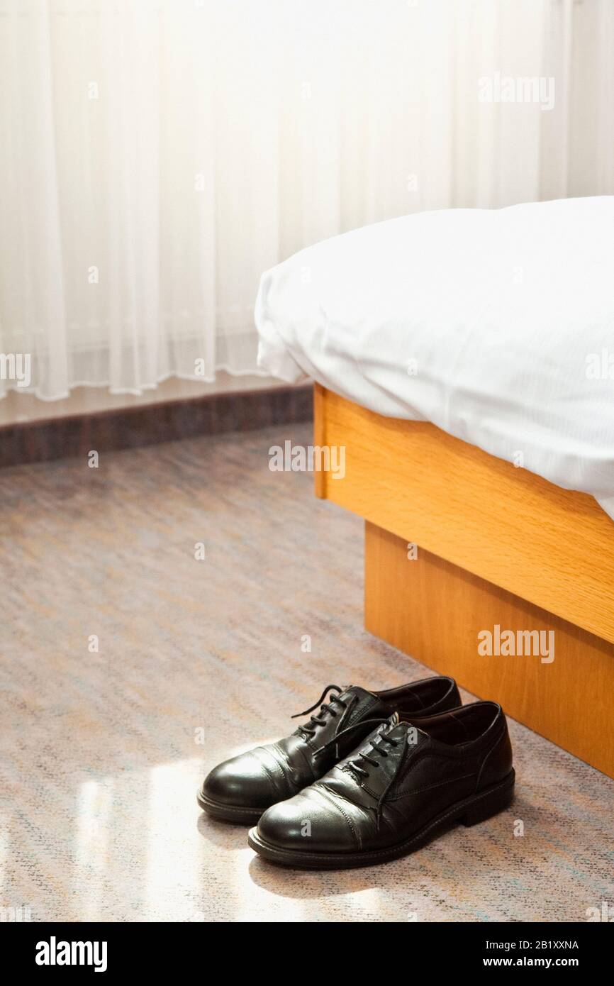 Paar schwarze Herrenschuhe am Ende eines Hotelbetts Stockfoto