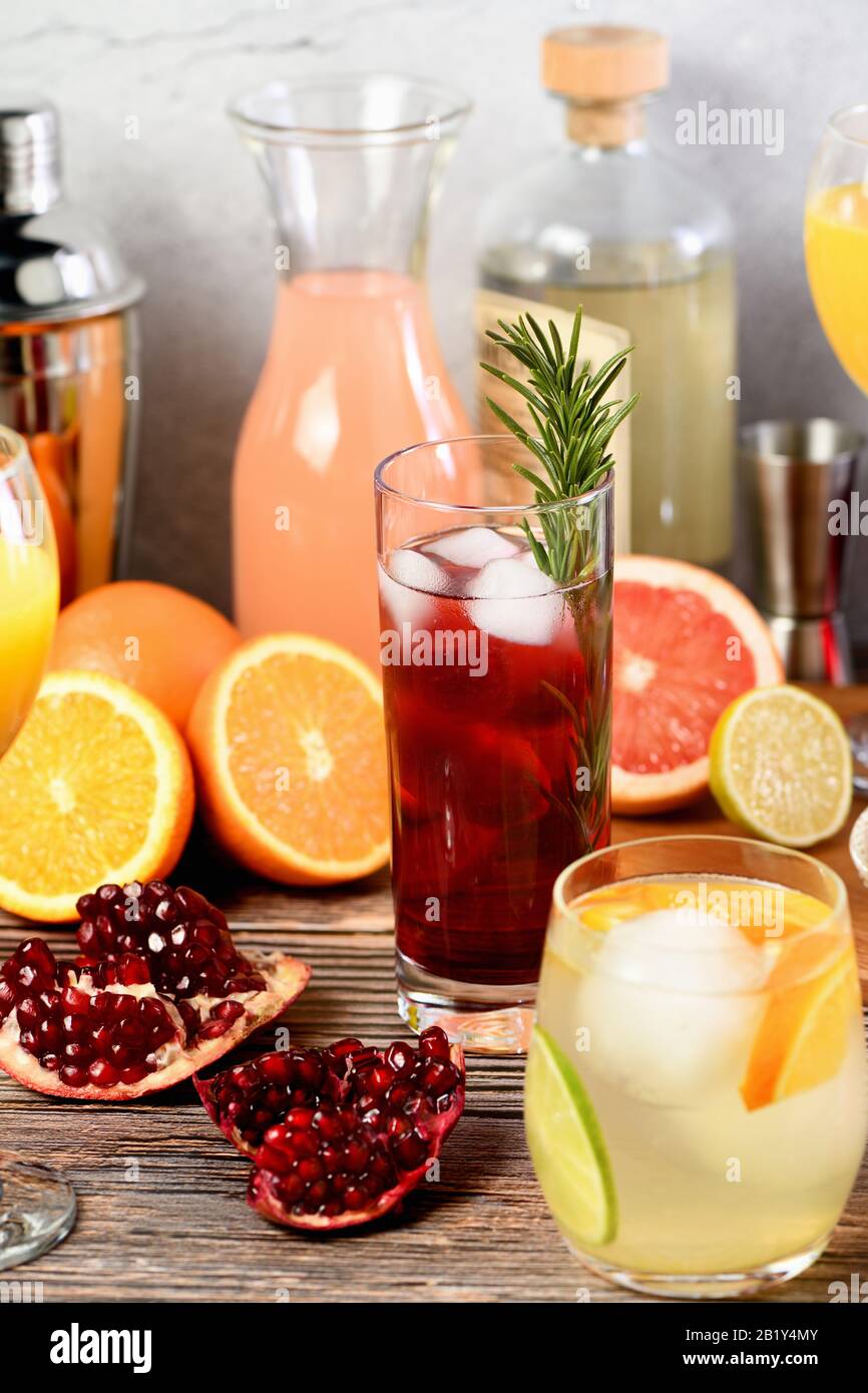 Gin-Cocktail mit Rosmarin und Granatapfel auf einem Tisch mit Zitrusfrüchten und Getränken. Stockfoto
