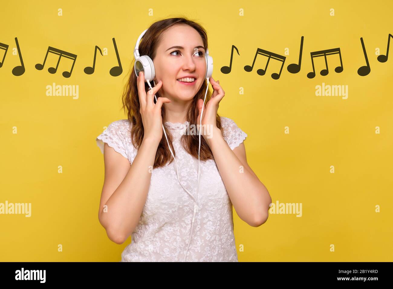 Ein Mädchen im Sommer steht auf einem gelben Hintergrund, hört Musik und abstrakte Noten kommen von den Kopfhörern. Nahaufnahme. Stockfoto