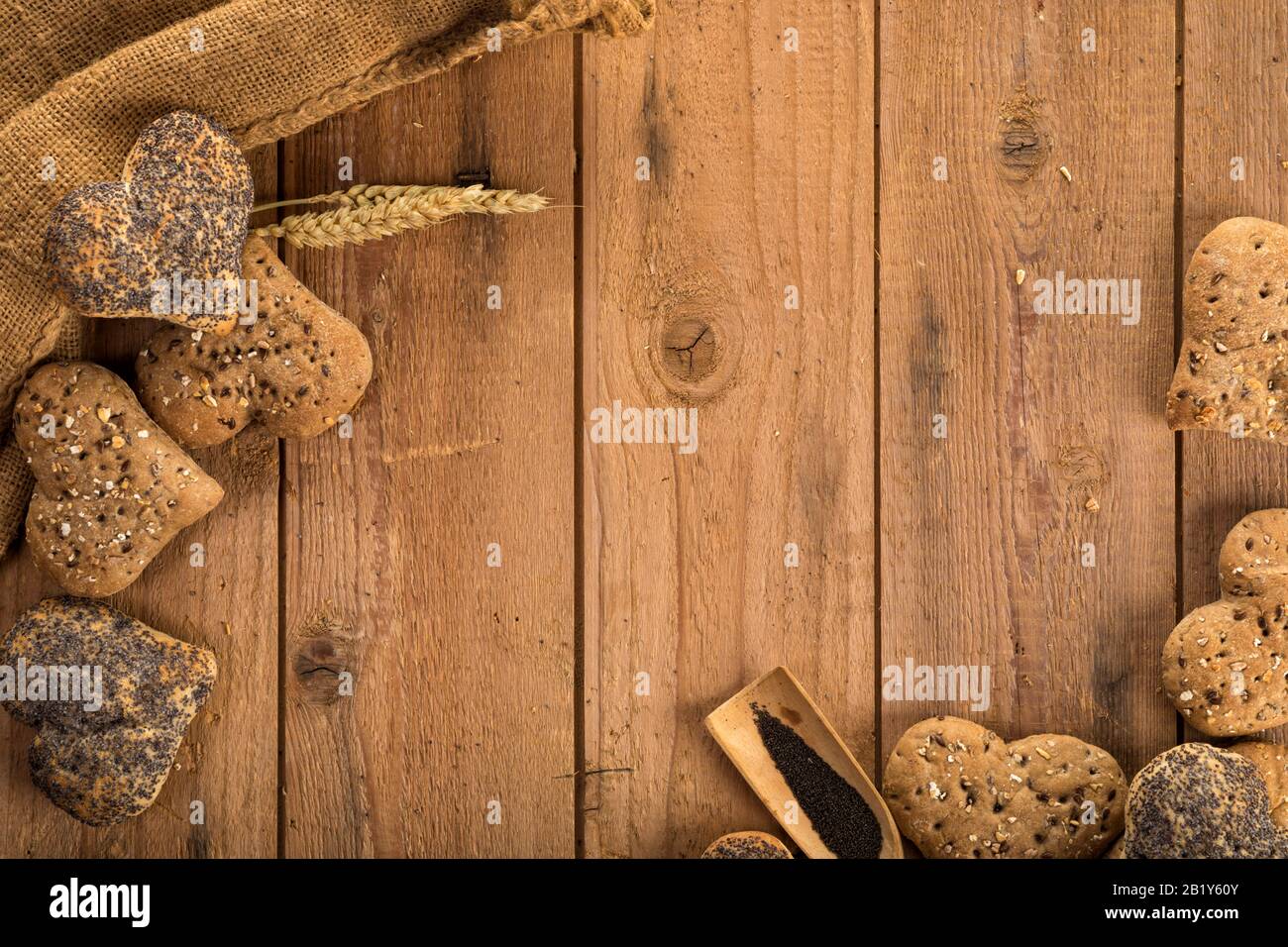 Hintergrund mit herzförmigen Brötchen, Körnern und Samen auf rustikalen Holzbohlen, großem Kopierraum Stockfoto