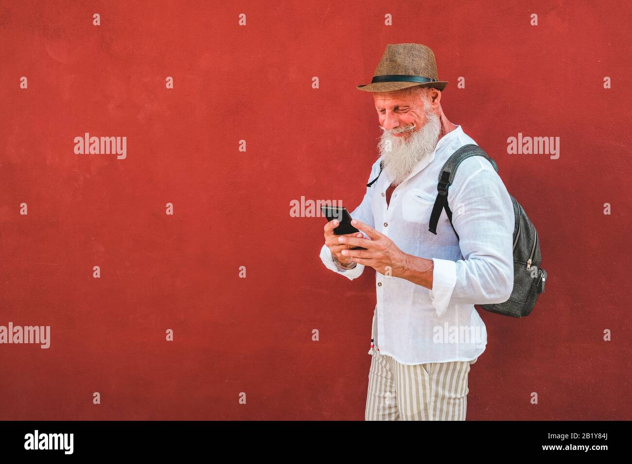 Trendiger Senior mit Smartphone-App mit rotem Hintergrund im Freien - Reifer Modemensch mit neuer Trendtechnologie - Tech, Reisen und Joyf Stockfoto