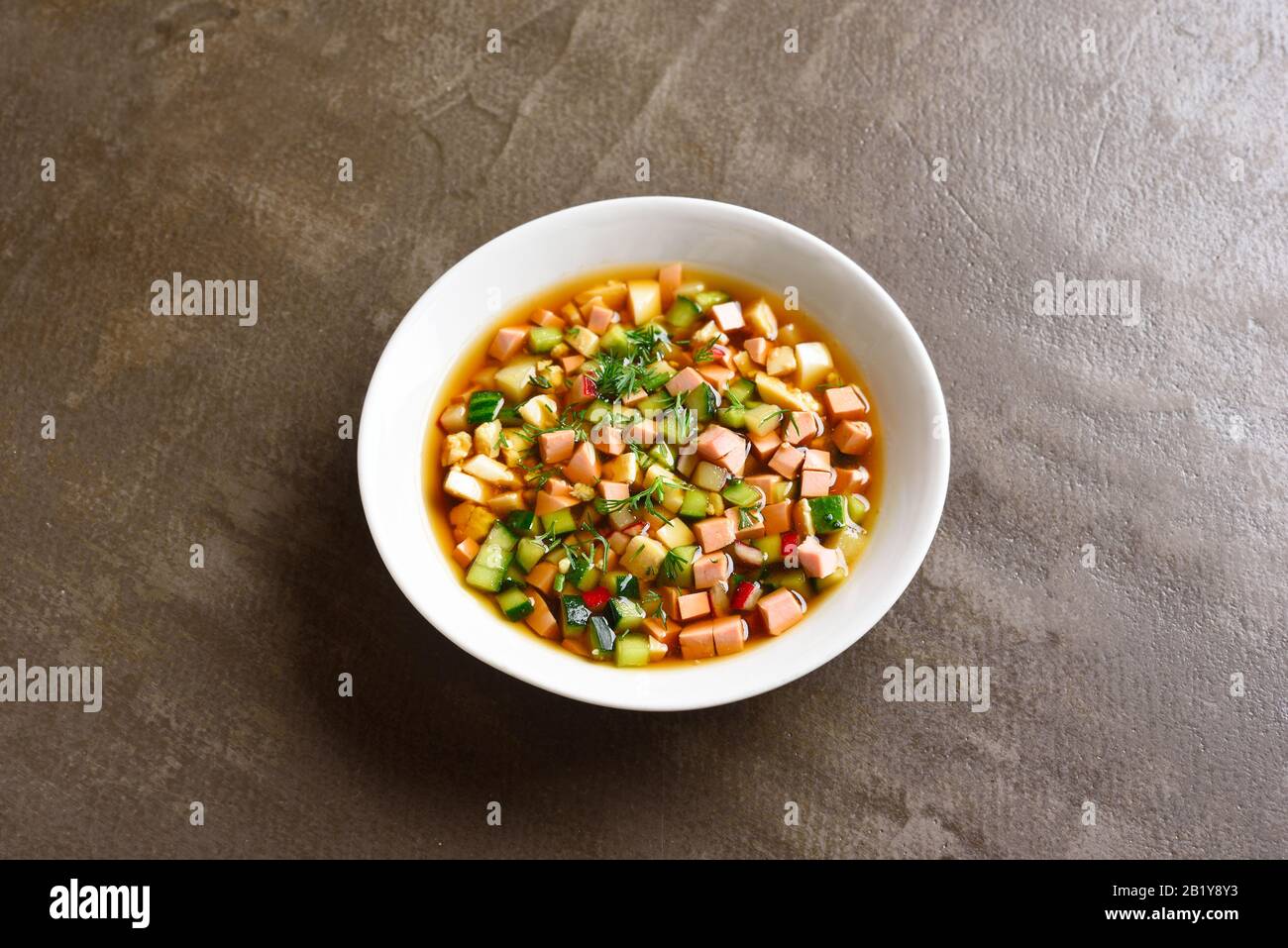 Nahaufnahme der kalten russischen Okroschka-Suppe mit Wurst, Gemüse und Kvass über braunem Steingrund mit freiem Textraum. Leckeres Sommergericht zum Abendessen Stockfoto