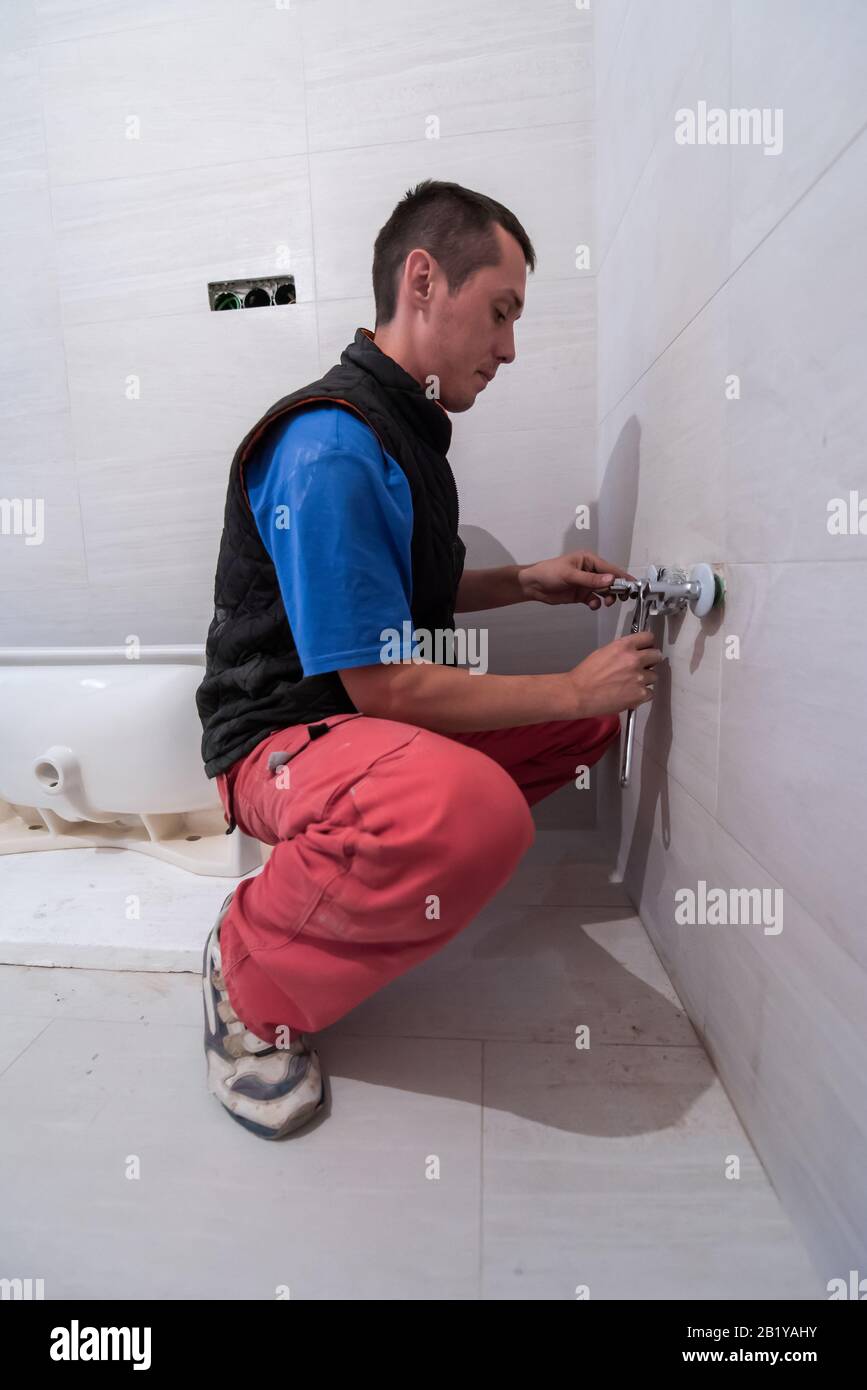 Professioneller Installateur, der in einem Bad arbeitet, Sanitäranlagen repariert, zusammengebaut und die Konzeptwerkzeuge und -Ausrüstung des Installateurs in einem Badezimmer installiert Stockfoto