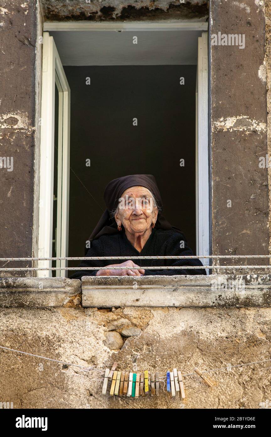 Eine alte Dame, in Schwarz gekleidet, blickt aus dem Fenster und beobachtet die Menschen. Scanno, Provinz l'Aquila, Abruzzen, Italien Stockfoto
