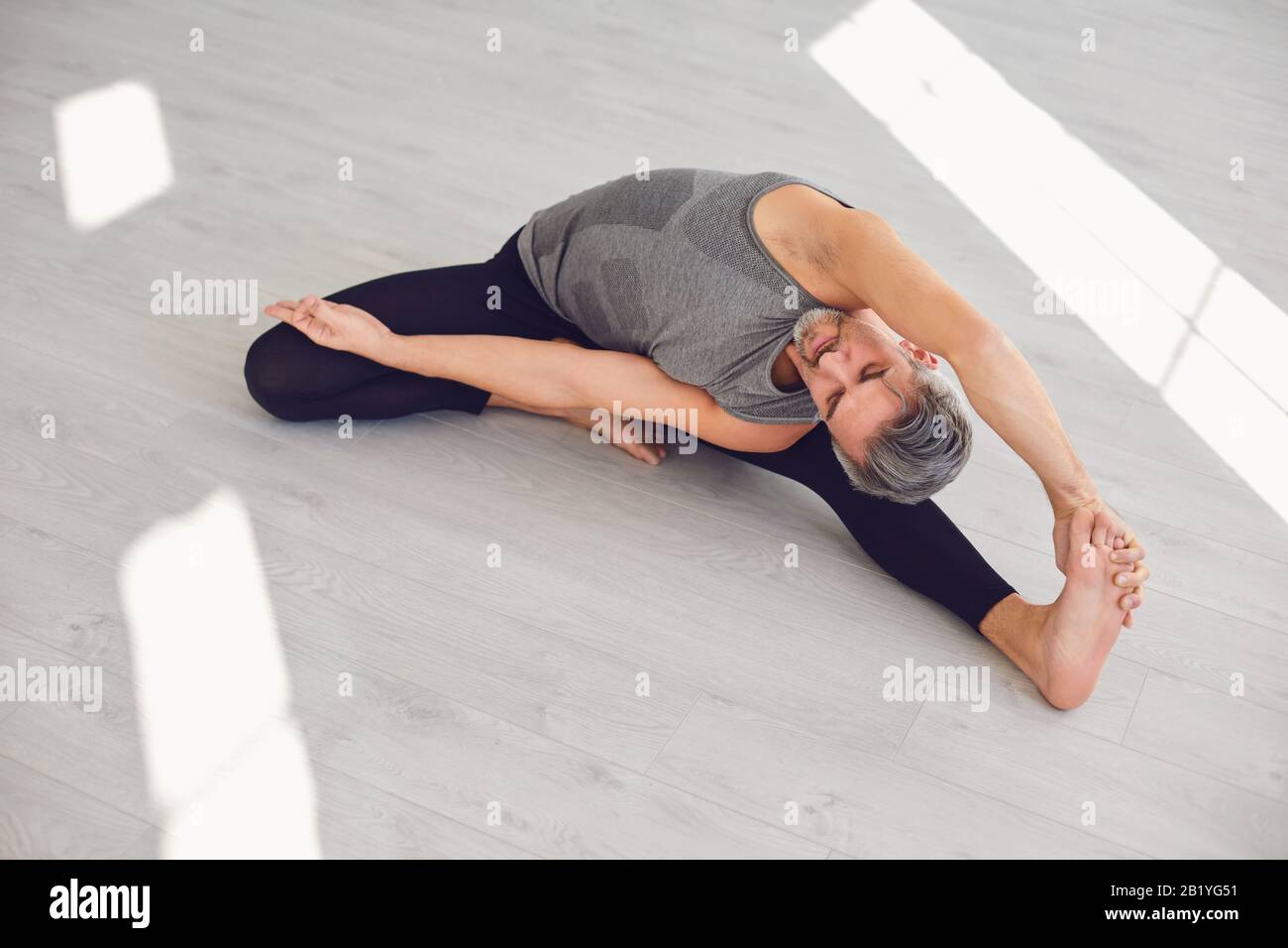 Yoga-Mann. Ein Mann übt Yoga-Balance in einem grauen Raum. Stockfoto