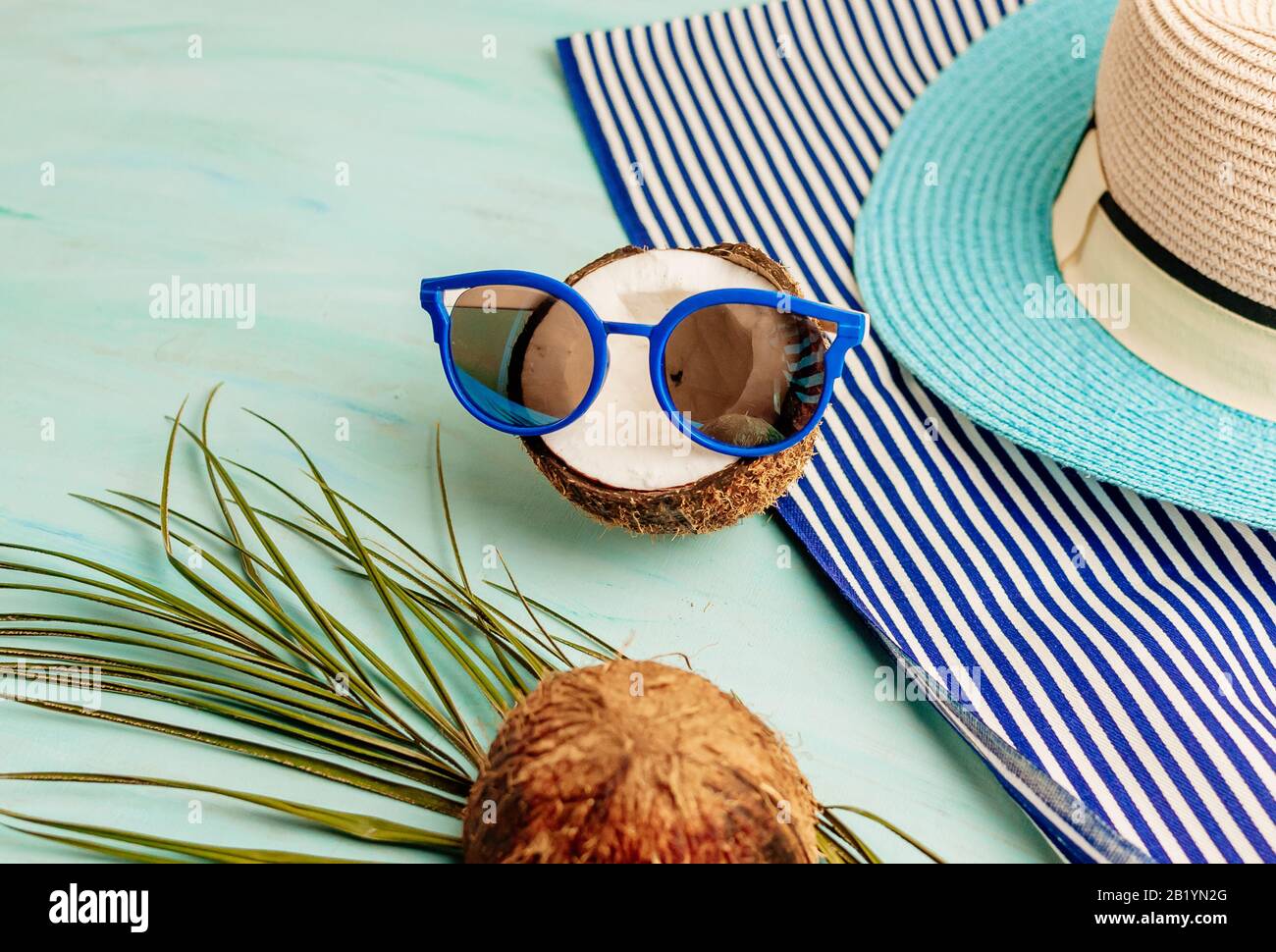 Komposition oder Layout im Sommer. Tropische Palmenblätter, Hut, Brille, Strandtuch, Kokosnuss auf dem Hintergrund von Meeresgrüns. Das Konzept der Sommersaison Stockfoto