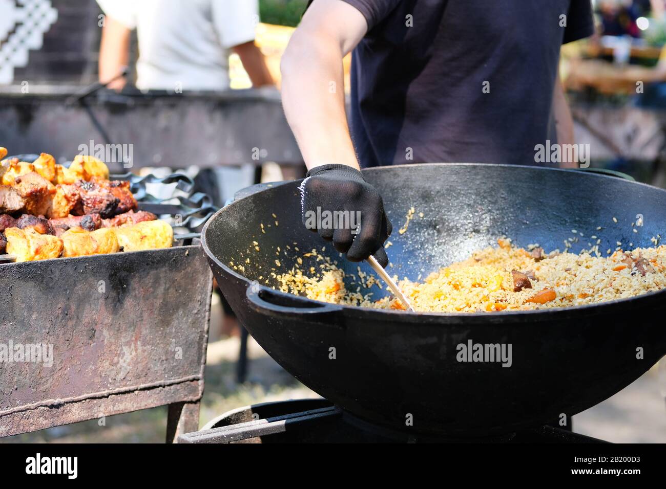 Zubereitung von Pilaf in großem schwarzen Gusseisen mit der Hand des Küchenchefs. Straßenküche und nationale Küche. Stockfoto