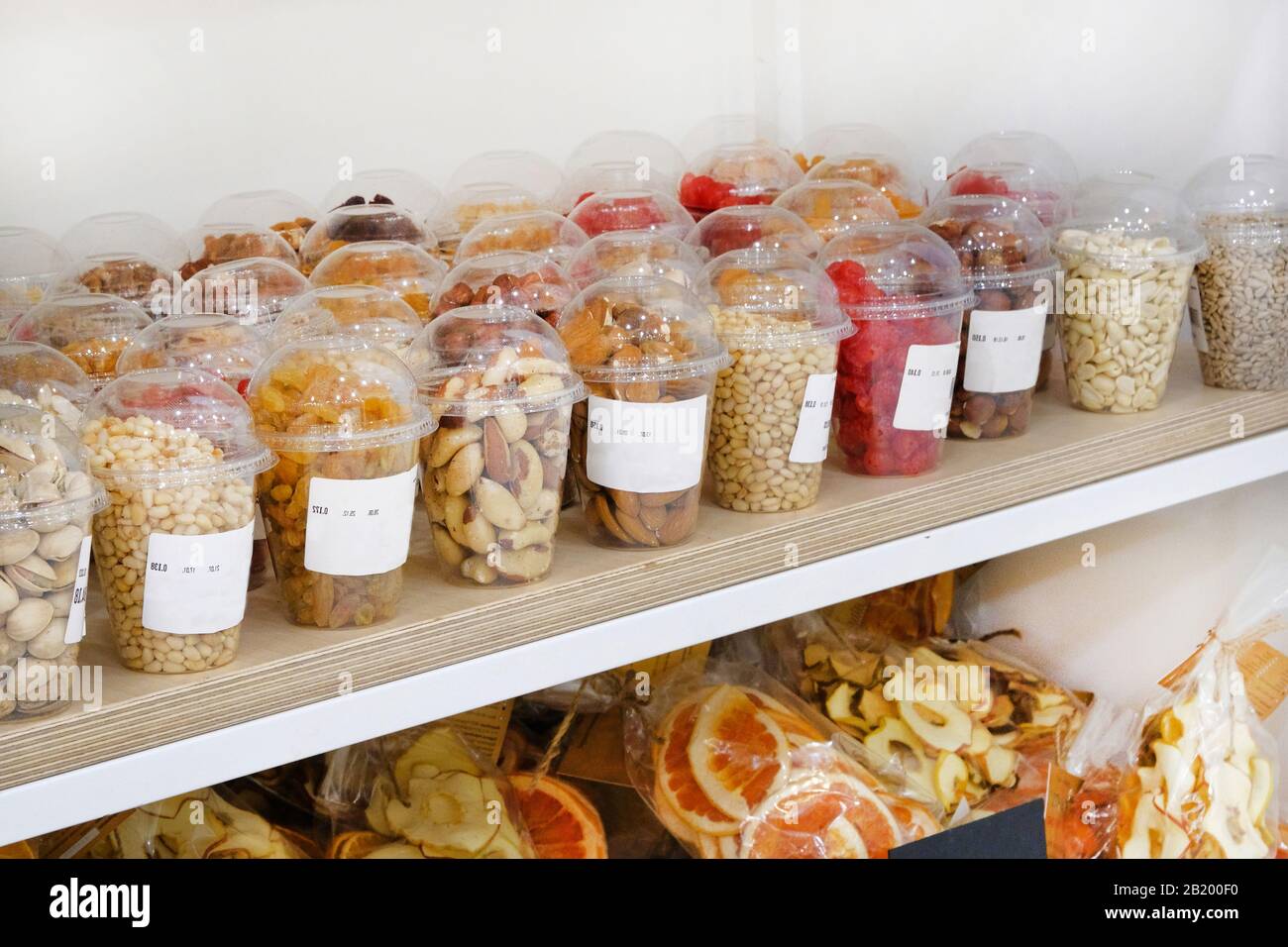 Verschiedene Nüsse und Samen in Plastikbechern: Mandeln, Haselnüsse, Zedernnüsse, Rosinen, Pistazien, Erdnüsse in Regalen auf veganem Markt. Stockfoto