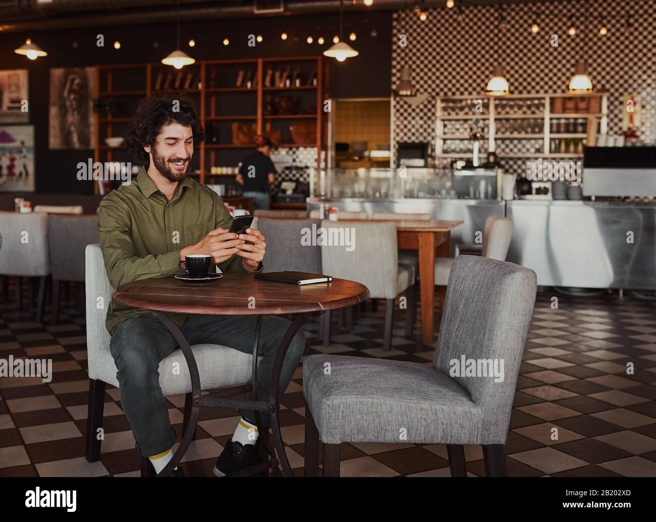 Fröhlicher kaukasischer junger Mann, der mit dem Handy im Café sitzt Stockfoto