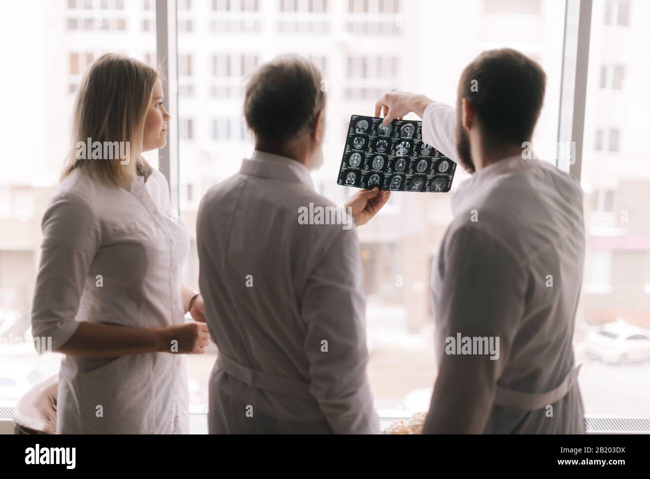 Das Team von drei Ärzten diskutiert die Röntgenaufnahme des Patienten im Beratungszimmer des Krankenhauses Stockfoto