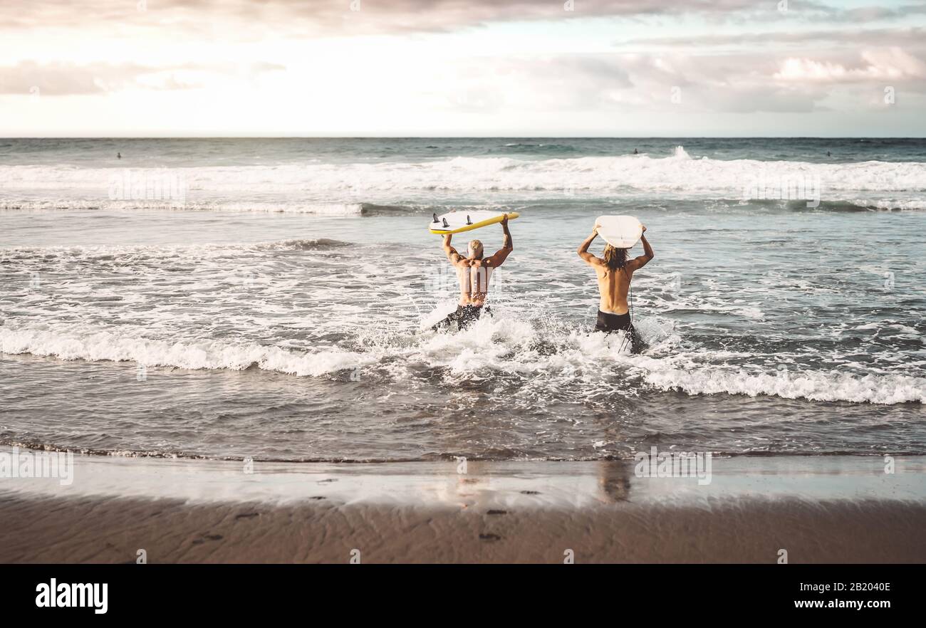 Freunde von Happy Fit haben Spaß beim Surfen während des Sonnenuntergangs - Leute, die Trainingsübungen in Schulsurfern machen Stockfoto