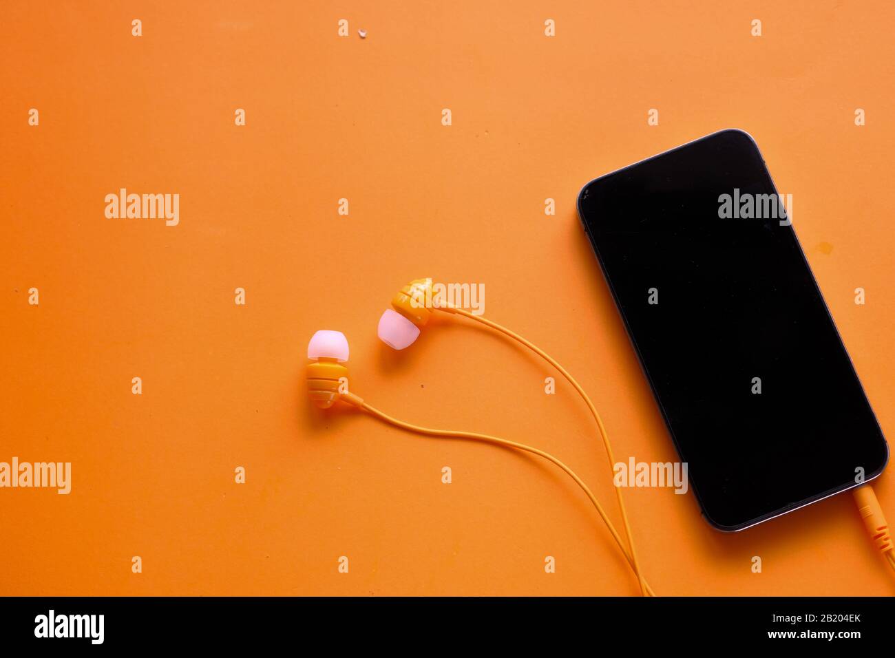 Obere Ansicht von Smartphone und Kopfhörer auf orangefarbenem Hintergrund Stockfoto