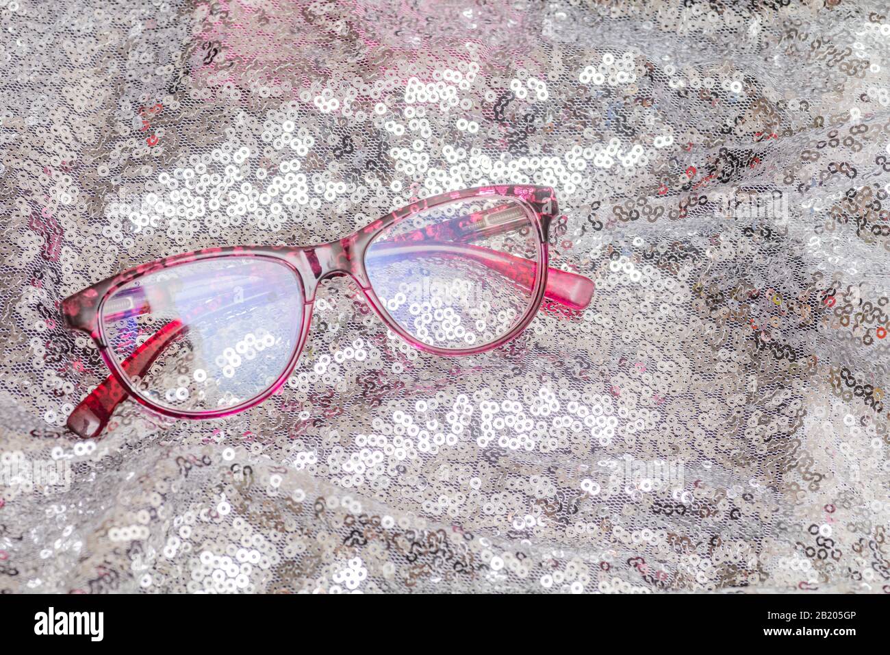 Eine billige Lesebrille mit pinkfarbenem Rahmen auf silberfarbenem Rücken Stockfoto