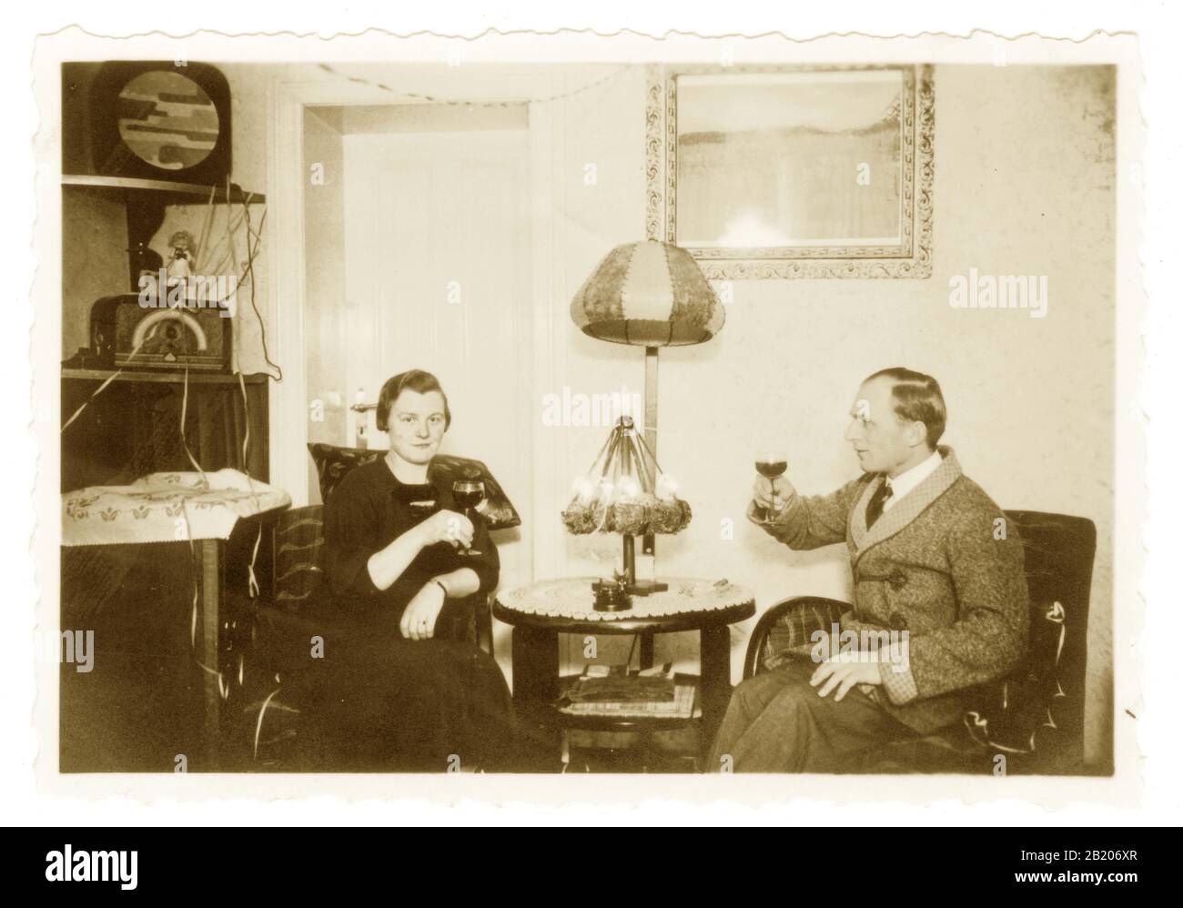 Anfang des 19. Jahrhunderts fotografierte ein Paar, das Weihnachten mit einem Getränk entspannen, Radio hören, Radio und Lautsprecher sind im Art-déco-Stil, überall Kabel, interessante Inneneinrichtung um die 1930er Jahre in den 1920er Jahren - unbekannte europäische Lage. Stockfoto