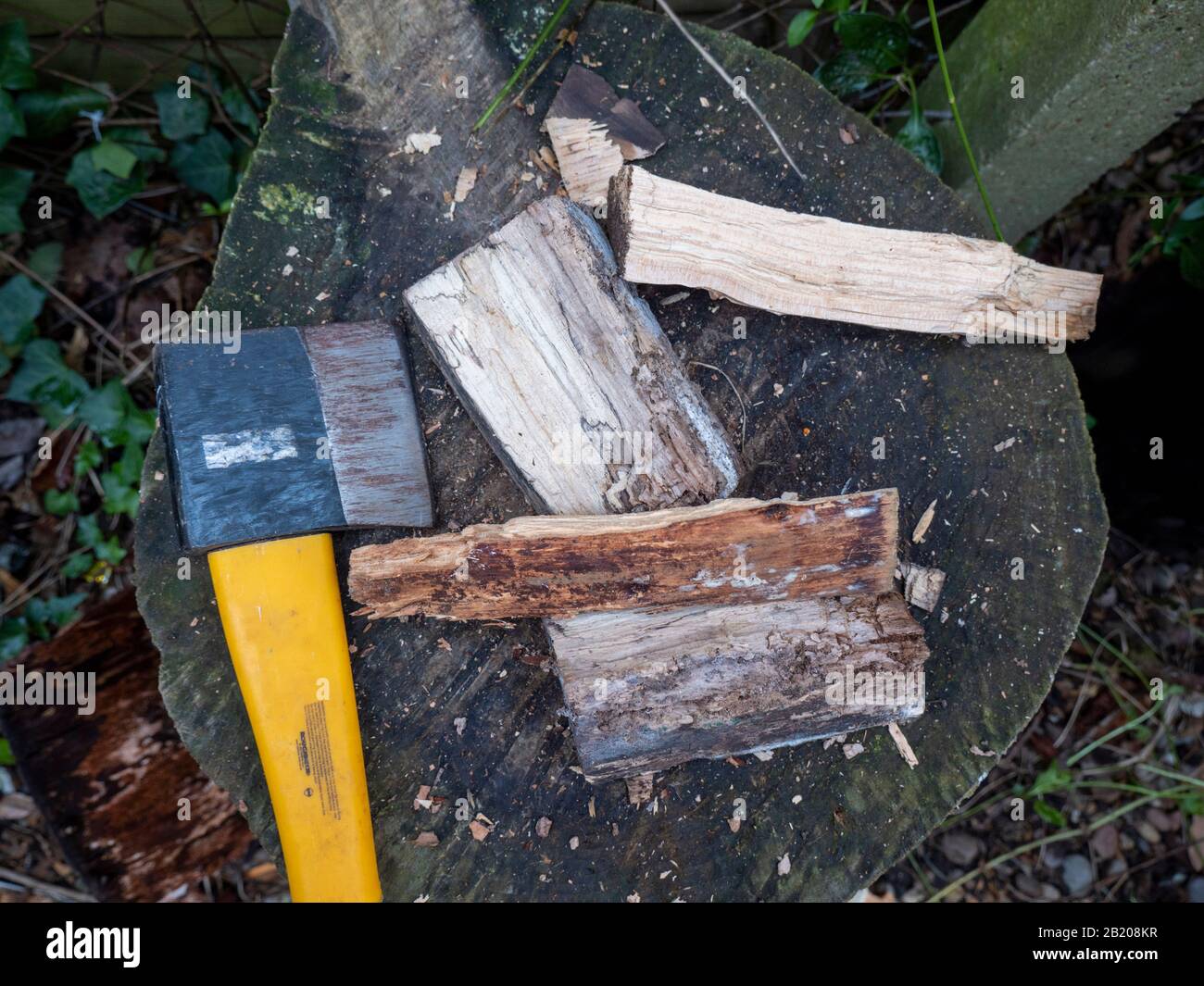 Eine Axt auf einem Hackblock mit gehacktem Anzünden von Holz, das bei einem Hausbrand zum Erhitzen brennt. Stockfoto