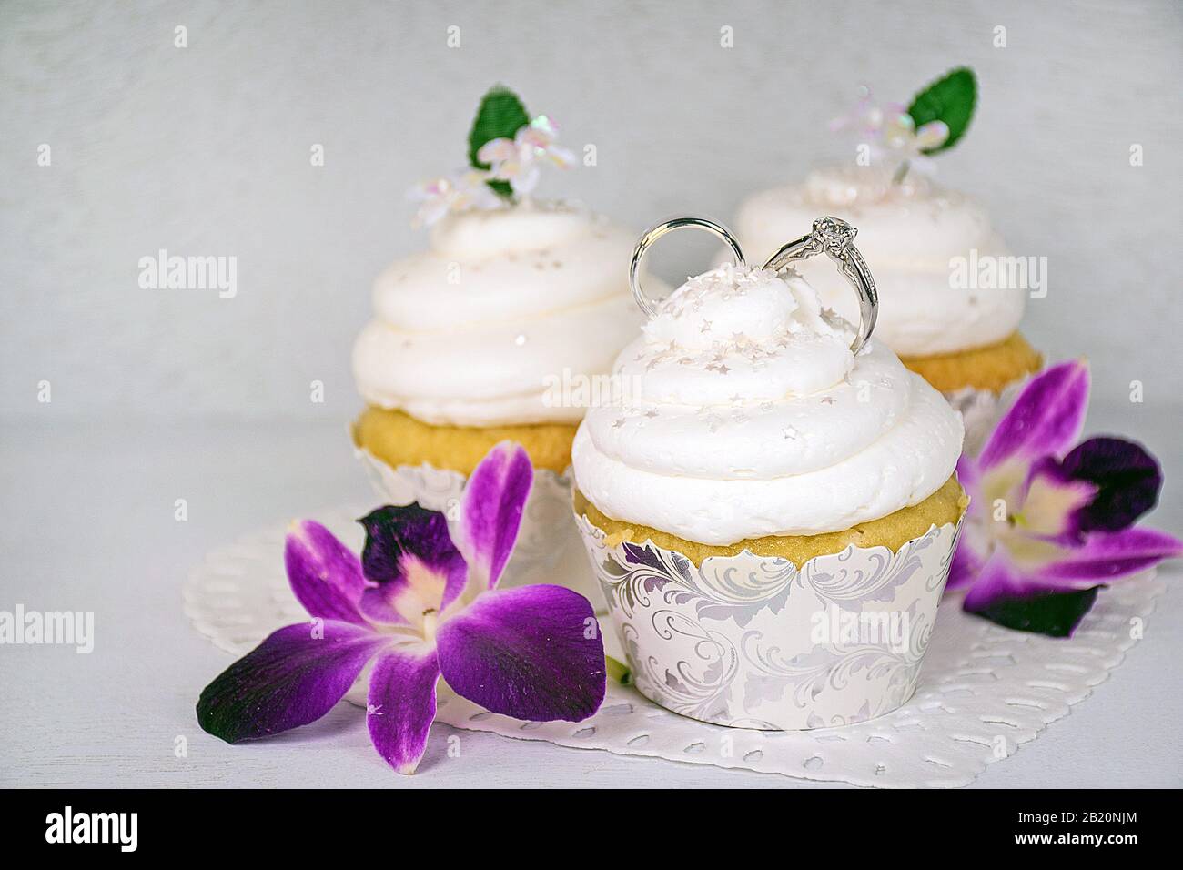 Hochzeitsringe in weißer Aufschäumung auf Cupcake mit Orchideenblüten Stockfoto