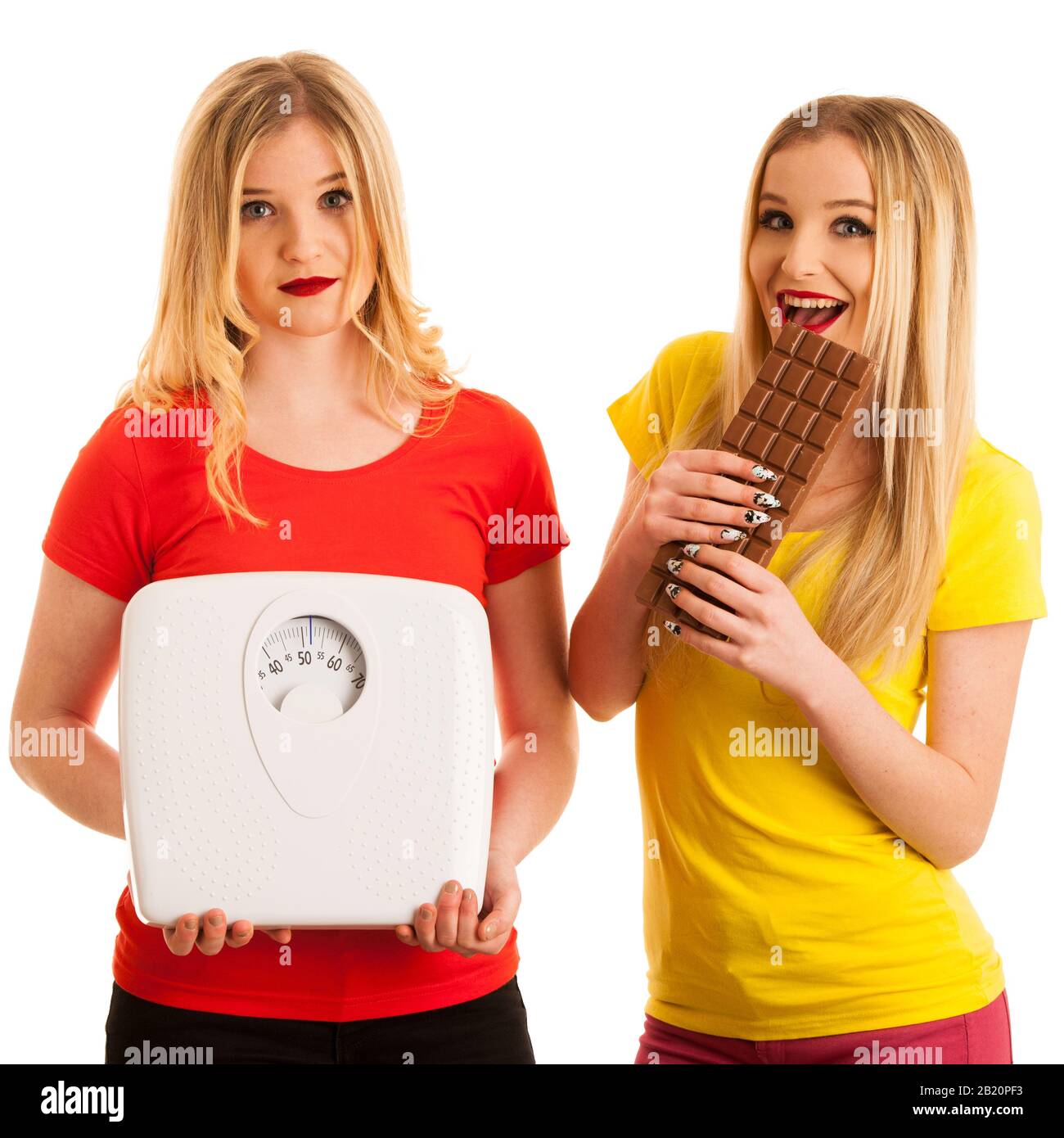 Fröhliche Frau, die Schokolade isst und Spaß an besorgter Frau hat, mit Skala isoliert über weiß Stockfoto