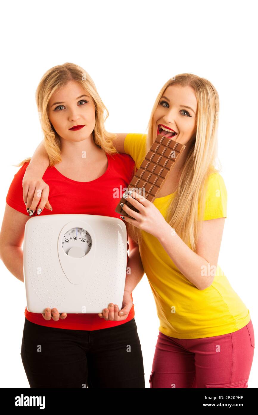 Fröhliche Frau, die Schokolade isst und Spaß an besorgter Frau hat, mit Skala isoliert über weiß Stockfoto