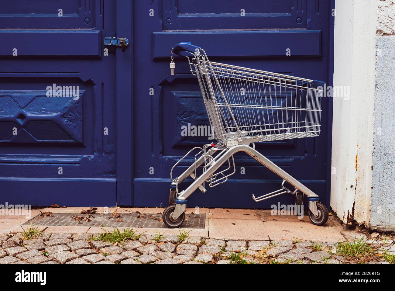 Vor einer großen blauen Eingangstür steht ein leerer Warenkorb Stockfoto