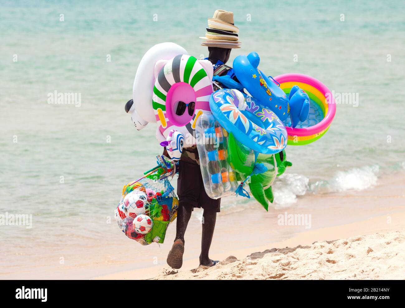 Ehrliches Bild von schwarzen Arbeitslosen, die am heißen Sommertag am Strand spazieren gehen und Spielzeug und Strandartikel verkaufen Stockfoto