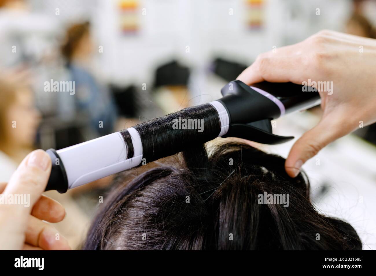 Haarstylist kräuselnde Haare aus nächster Nähe. Friseursalon zum Braunen langer Haare Frau im Schönheitssalon. Professionelle Haarpflege, Haarkleiden Stockfoto
