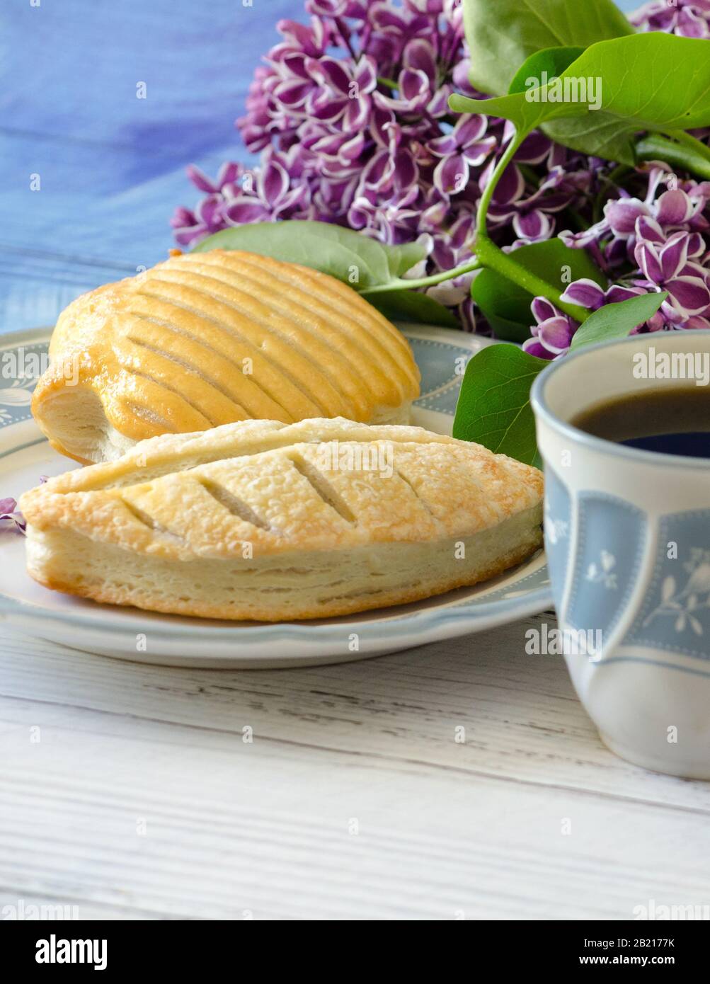 Puffgebäck auf dem Teller ist mit Kaffee und einem Blumenstrauß aus Flieder für ein angenehmes leichtes Frühstück kombiniert Stockfoto