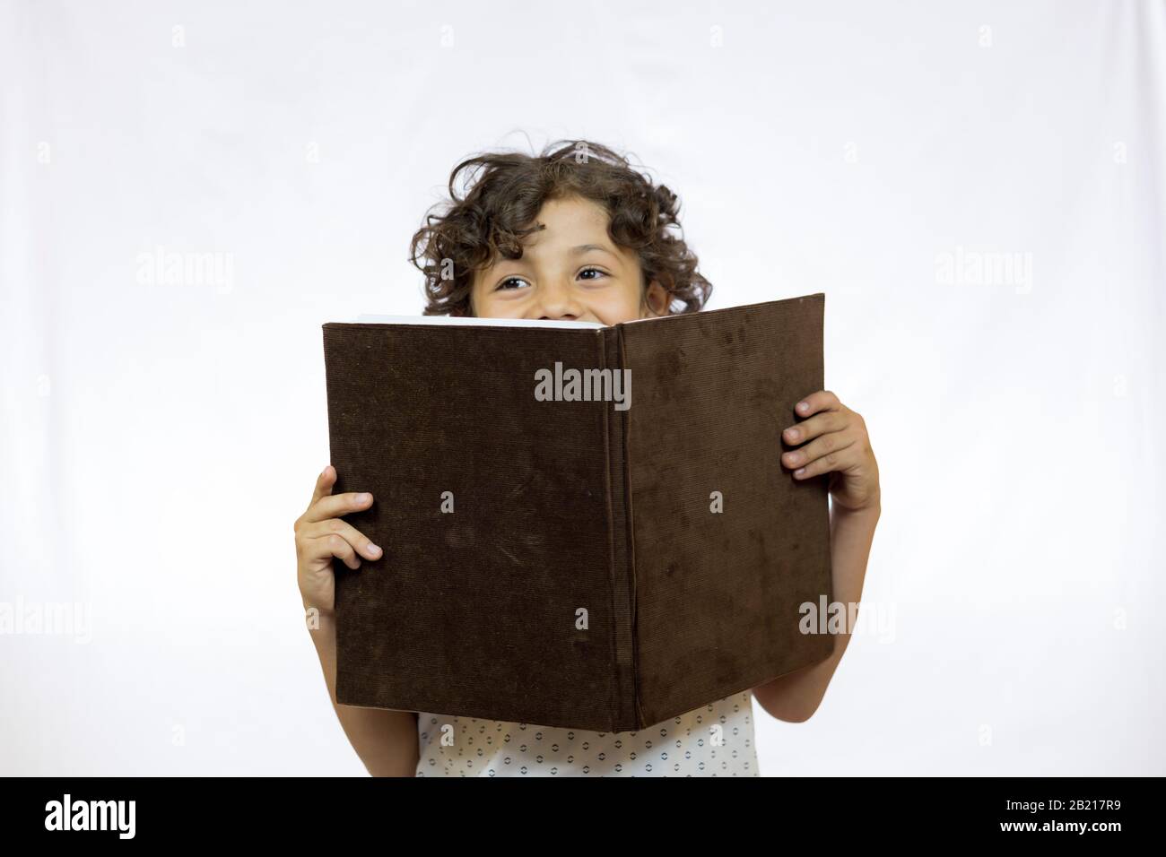 Lächelnder Junge zwischen 8 und 9 Jahren, der ein Buch hält, während er es liest und vor weißem Hintergrund steht Stockfoto