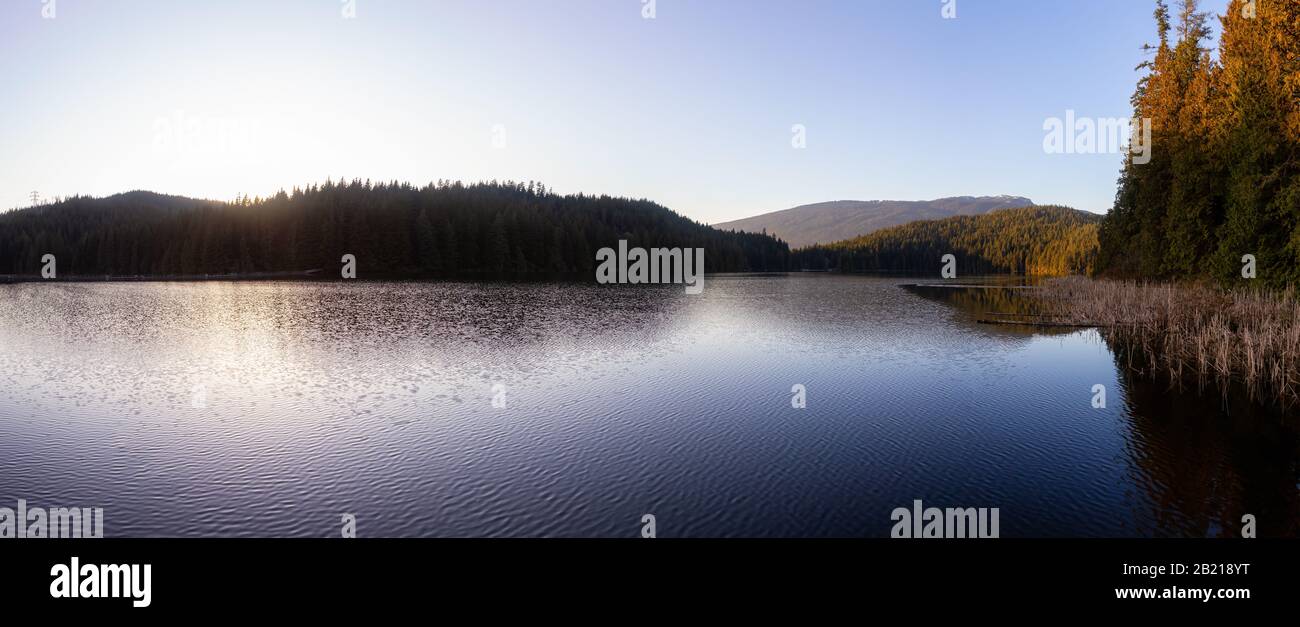 Schöner und Lebendiger Panoramablick auf einen See, der bei Sonnenuntergang von der kanadischen Berglandschaft überragt wird. Aufgenommen in White Pine Beach, Port Moody, Vancouver Stockfoto