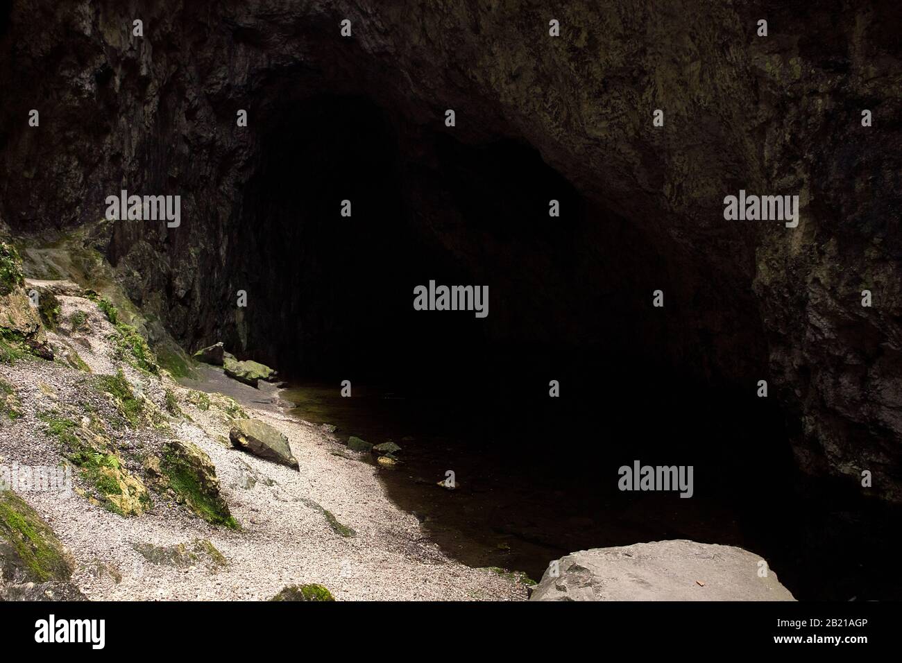 Malerische Landschaft in der U-Bahn. Ufer eines unterirdischen Sees, der von Felsen umgeben ist. Dunkelheit im Höhlenkorridor und Licht, das auf die Bank fällt. Speläologie Backgr Stockfoto