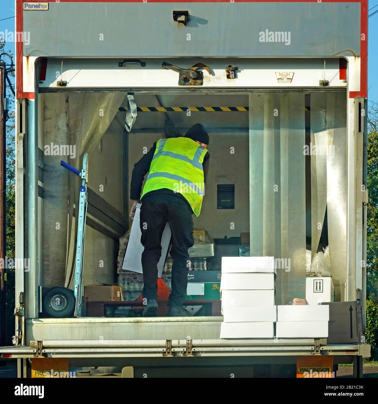 LKW-Fahrer in hoher Vis-Jacke hinter seinem Lieferwagen vor dem Geschäft geparkt Sortierboxen & Pakete auf Heckgatter-Hydrauliklaufwerk England UK Stockfoto