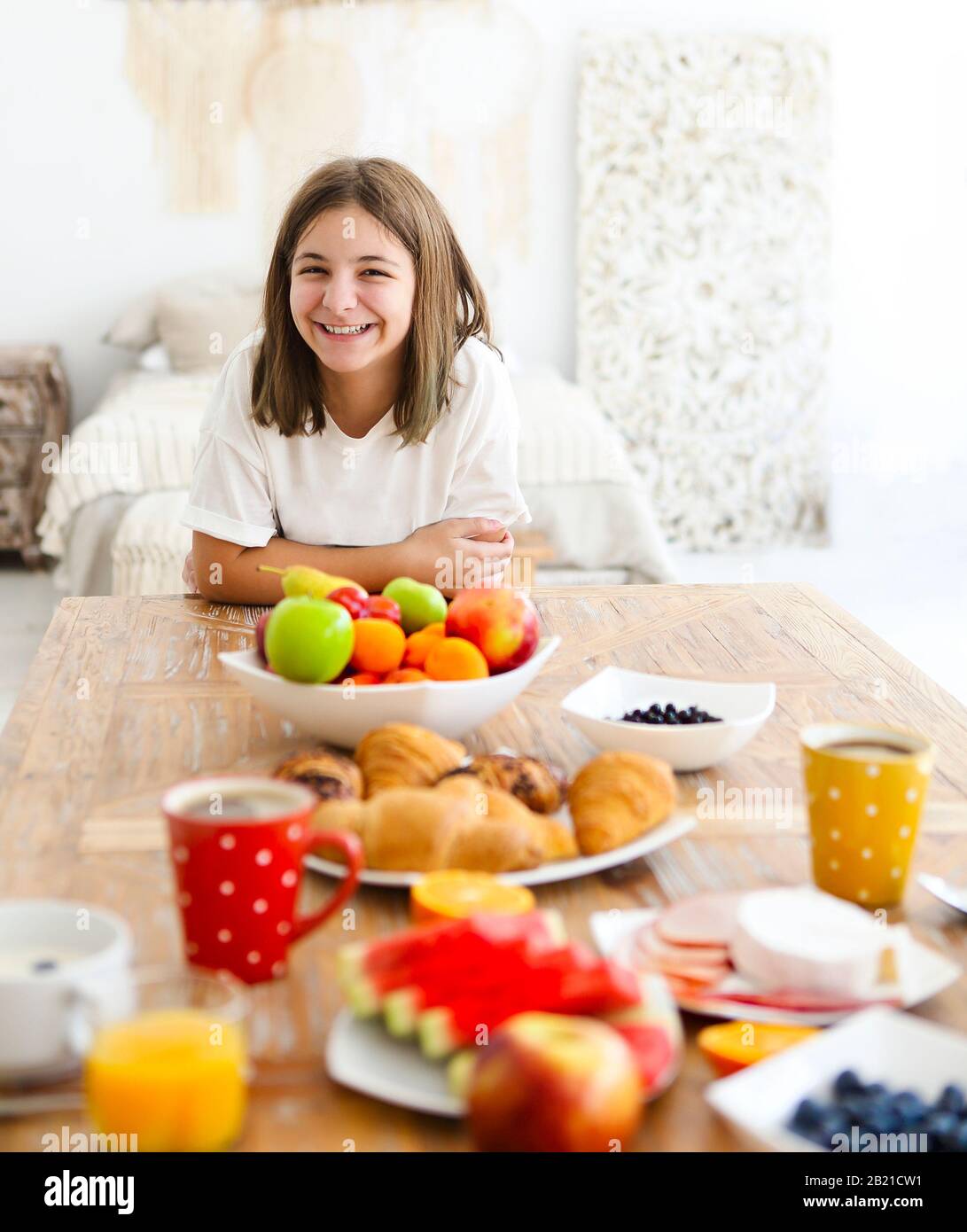 Von oben ein glückliches Mädchen in weißem T-Shirt, das mit strahlendem Lächeln am Tisch mit köstlichem Frühstück auf die Kamera blickt Stockfoto
