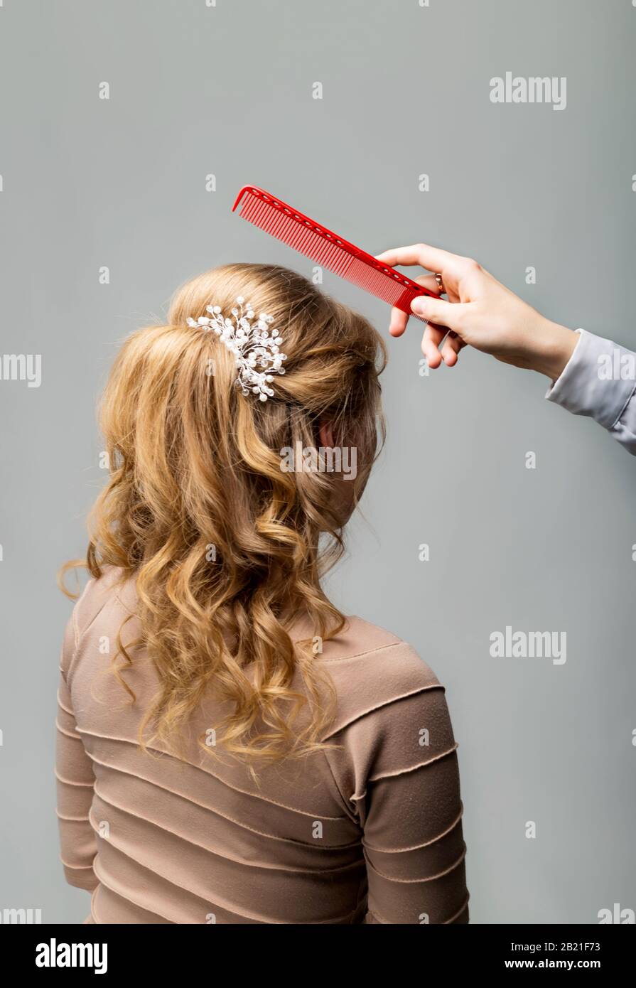 Wellen Locken Frisur. Friseursalon blonde Haarfrau mit langen Haaren mit Kamm auf grauem Hintergrund. Professionelle Frisur Stockfoto