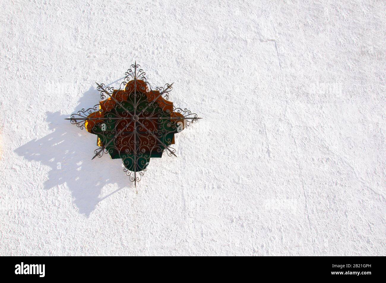 Buntes Buntglasfenster mit gemustertem Schmiedegitter an der weißen Wand. Spanischer Stil Stockfoto