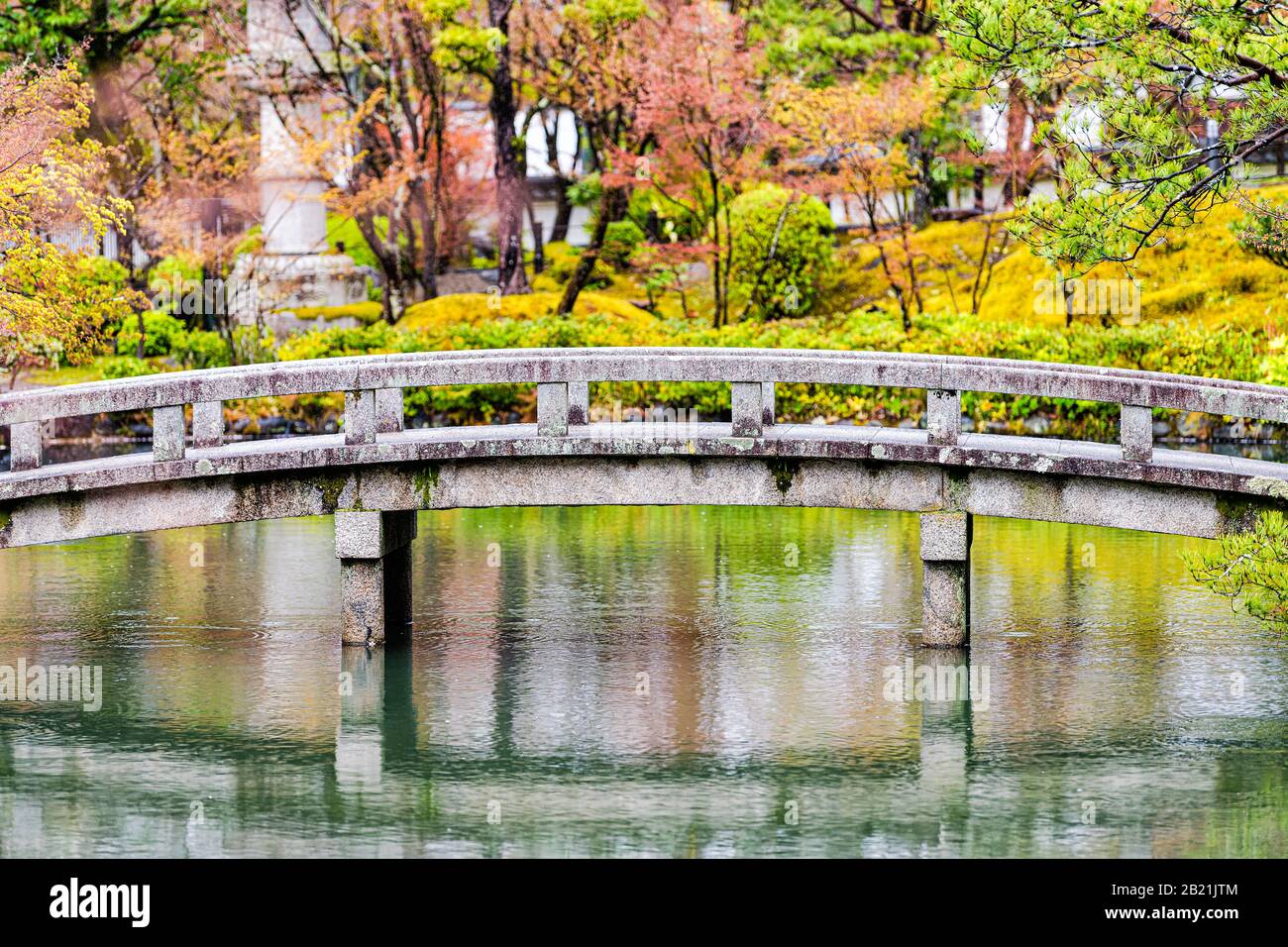 Eikando-Tempelsteinbrücke in der Gartenreflexion in Kyoto, Japan im Frühjahr mit grünen und orangefarbenen Bäumen und Gebäuden Stockfoto
