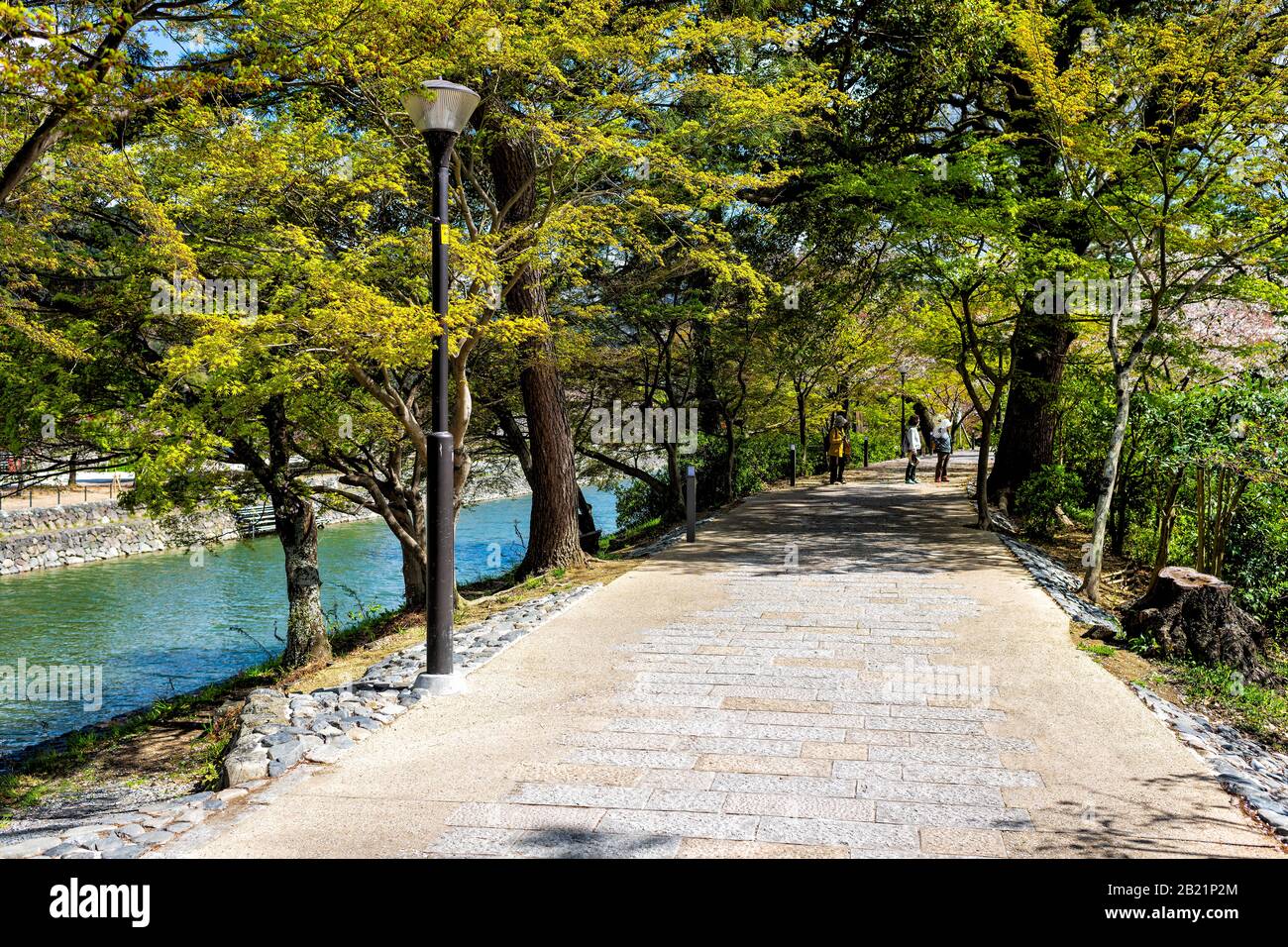 Uji, Japan - 14. April 2019: Pfad im Frühling im traditionellen Dorf mit Menschen, die an Kirschblütenbaum und Fluss laufen Stockfoto