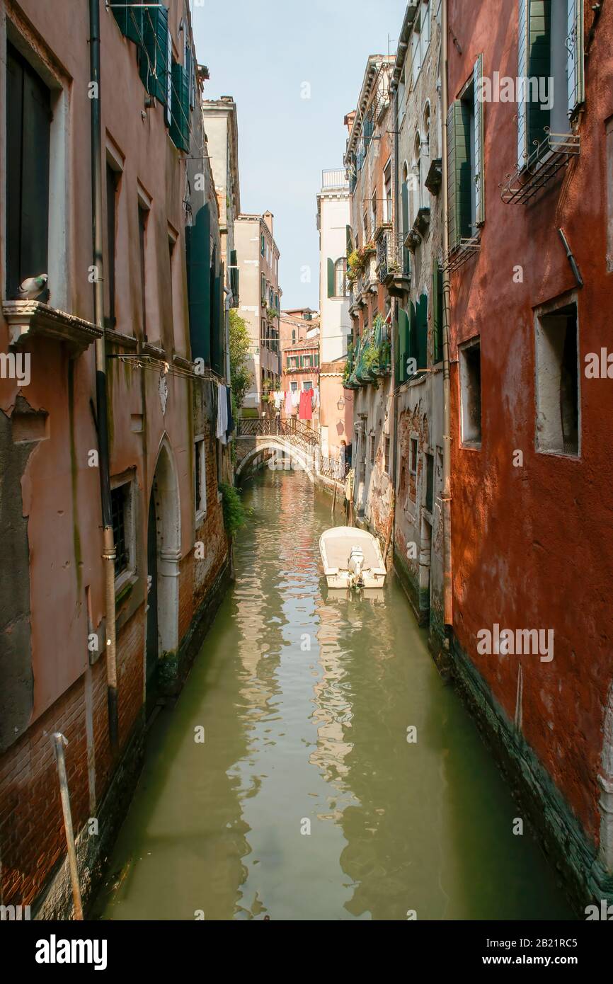 Ein kleiner Seitenkanal mit Gebäuden, Boot und Brücke. Wäsche kann in der Ferne trocken gesehen werden. Venedig, Italien. Stockfoto