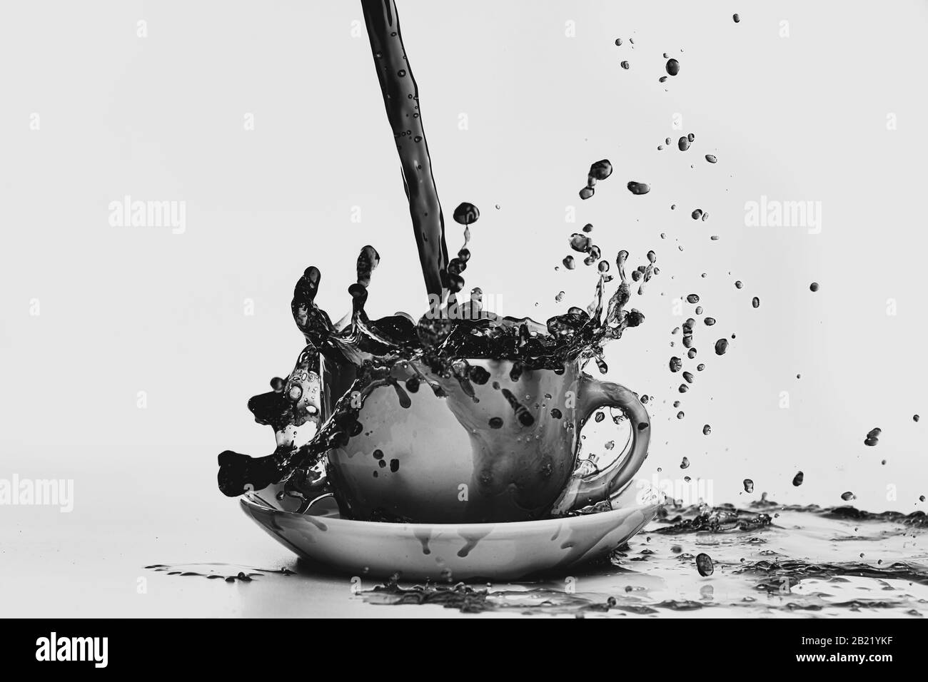 Schwarzweißfoto von Kaffee, der in eine weiße Tasse gießt, die vor einem einfarbigen weißen Hintergrund isoliert ist und in alle Richtungen spritzt, was zu einem Chaos führt Stockfoto