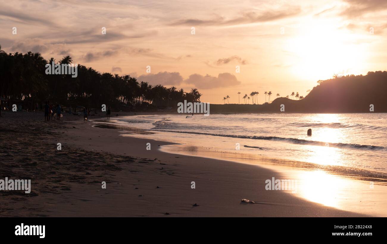 Sanfte Wellen waschen sich bei Sonnenuntergang über einem topischen Meeresstrand. Ruhige Wellen des Meeres am Sandstrand bei Sonnenuntergang. Sonnenspiegelung im Meerwasser. Stockfoto