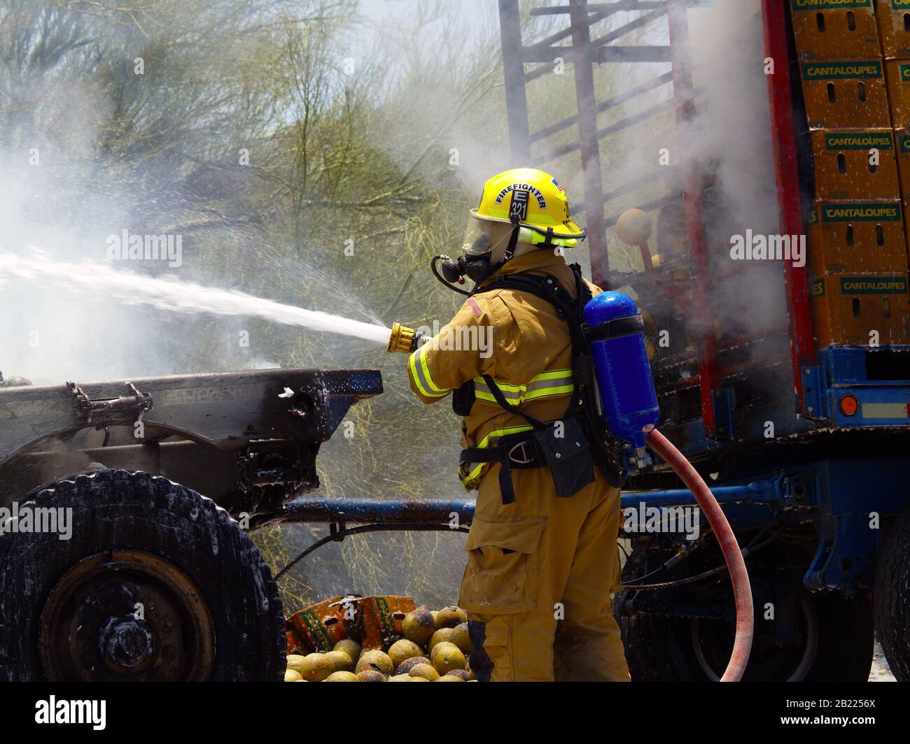 Ein Feuerwehrmann, der einen Fahrzeugbrand entlang einer Straße in Arizona löscht. Das Gesicht des Feuerwehrmannes ist nicht sichtbar, eine Modellfreigabe ist nicht erforderlich. Stockfoto