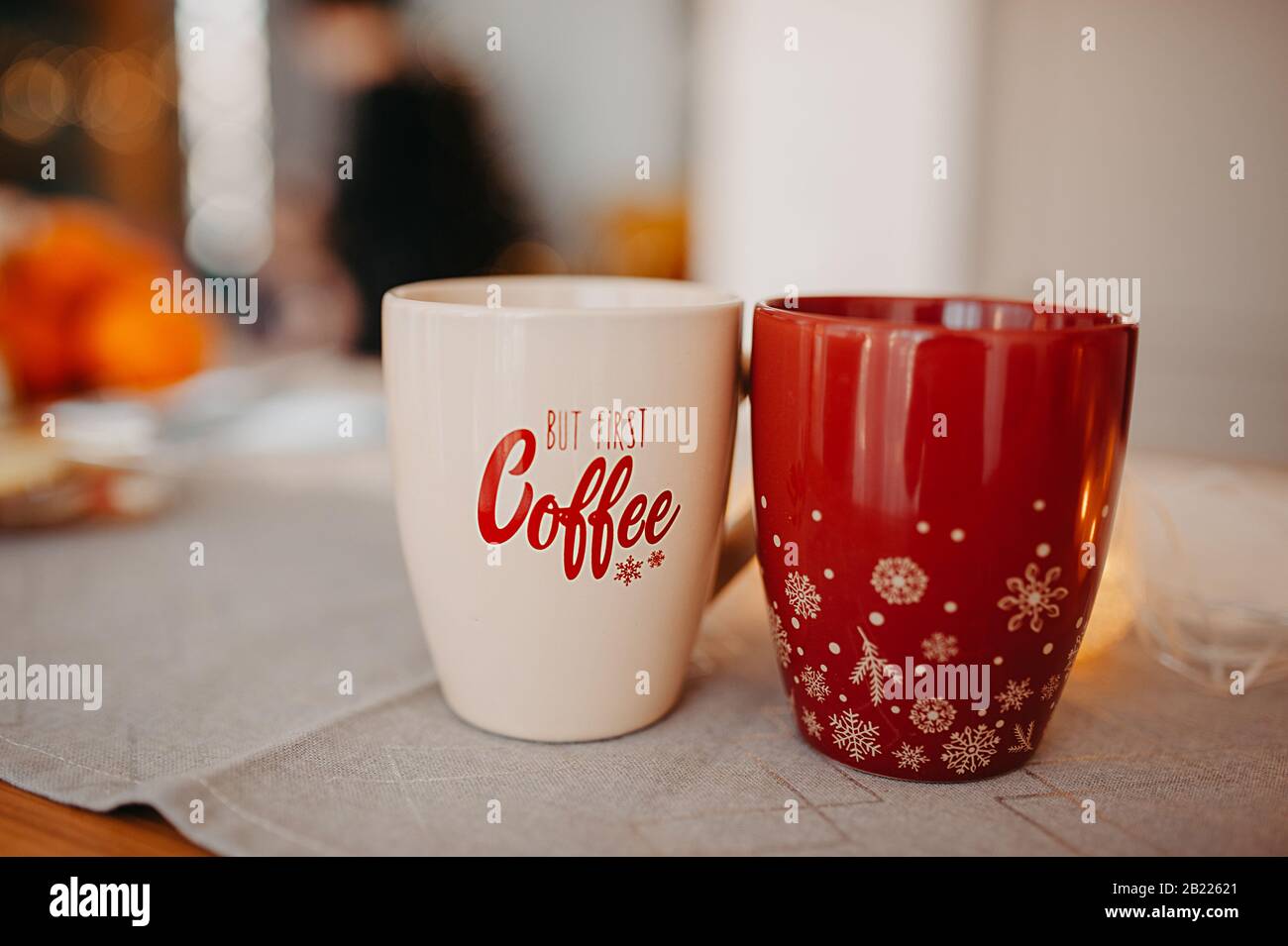 Zwei Weihnachtsbecher auf einer Baumwoll-Serviette in der Küche, ein beigefarbener Becher mit der Aufschrift über Kaffee, ein roter Becher mit Schneeflocken Stockfoto